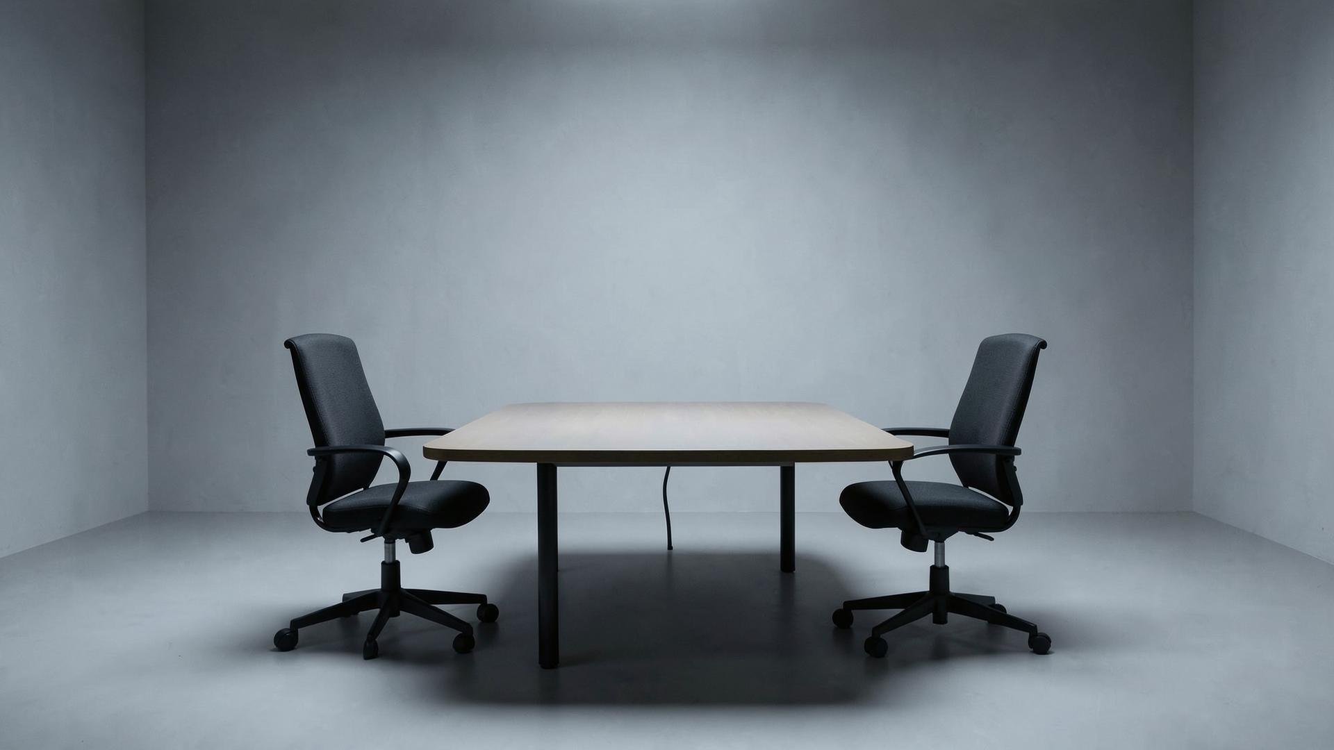Mesa de negociación vacía con dos sillas en una sala gris