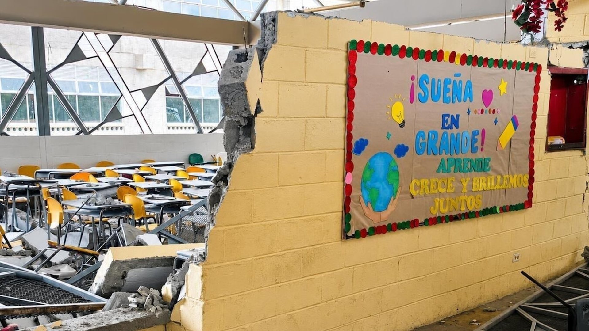 Aula escolar con muros agrietados y pupitres apilados tras el sismo